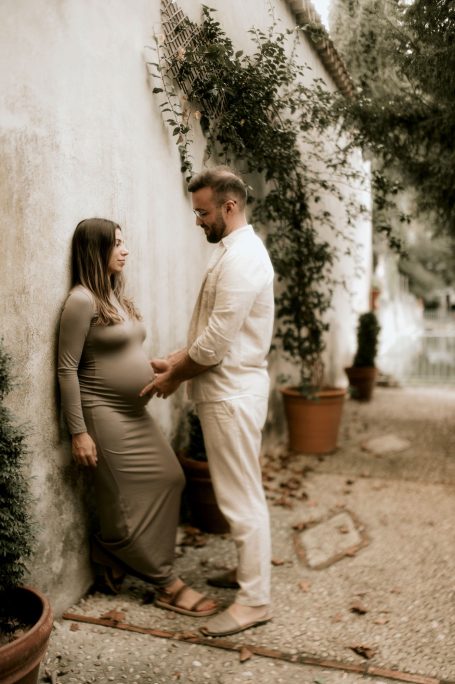 Pareja embarazada posando junto a una pared y plantas en un entorno natural.