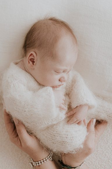 Bebé dormido envuelto en un suave suéter blanco, sostenido con cuidado en manos.