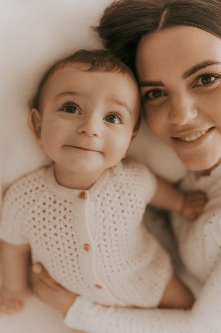 Mujer sonriente abrazando a un bebé feliz con un suéter de punto claro.