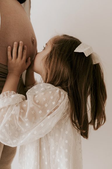 Niña besando una barriga de embarazada, en un entorno suave y cálido.