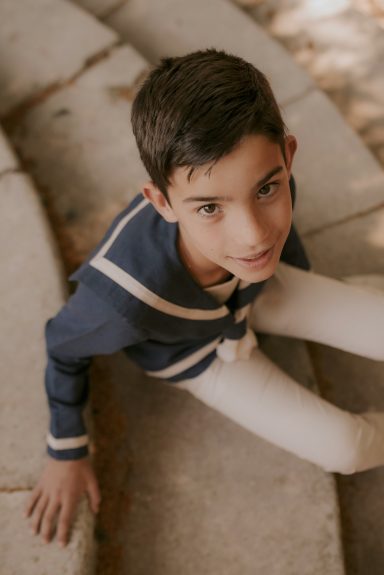 Niño sentado en una escalera, mirando hacia arriba, con camiseta azul y pantalones claros.