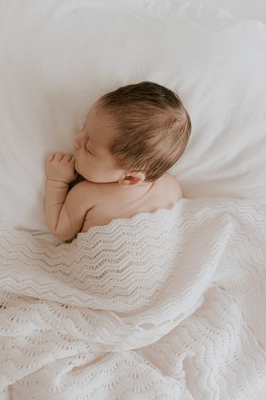 Bebé dormido envuelto en una manta blanca, acostado de espaldas sobre sábanas suaves.