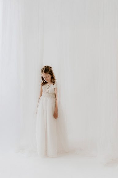 Niña con vestido blanco en un fondo claro, sonriendo suavemente.