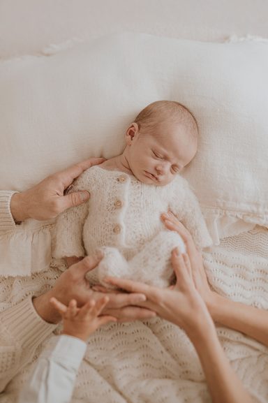 Bebé dormido en una cama, rodeado de manos que lo sostienen con ternura.