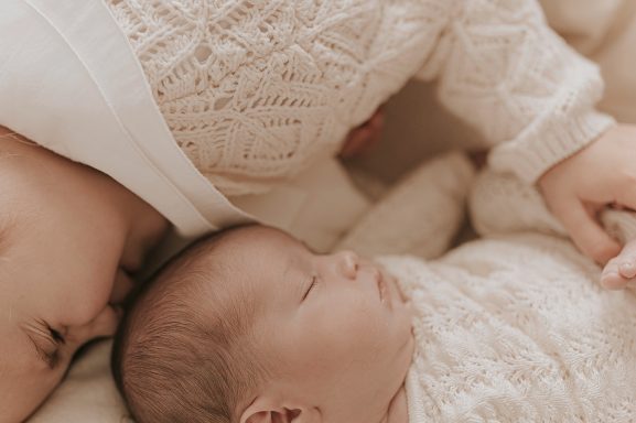 Niño abrazando a un bebé dormido, ambos visten suéteres de punto claros.