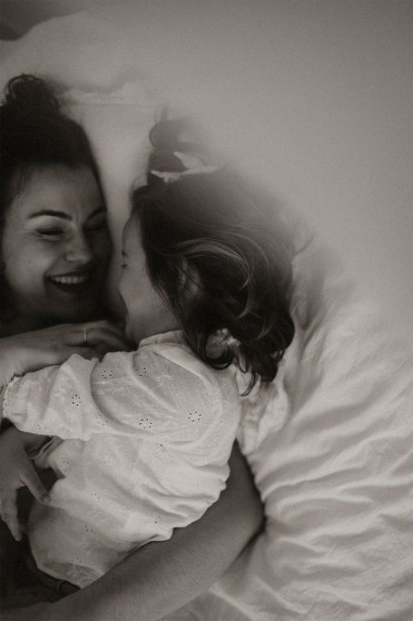 Mujer y niña se abrazan y sonríen en una cama, mostrando un momento de ternura.