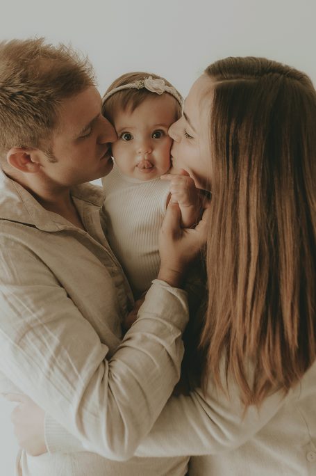 Padres besando a su hija pequeña en un entorno cálido y acogedor.