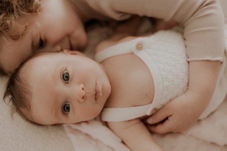 Un niño pequeño abraza a un bebé acostados sobre una superficie suave.