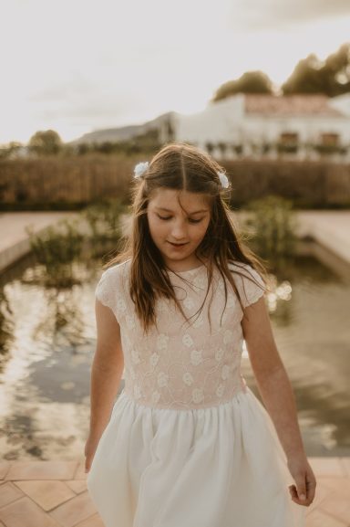 Niña caminando cerca de un estanque, con un vestido blanco y cabello largo.