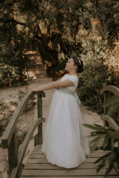Mujer con vestido blanco de boda en un puente rodeado de naturaleza.