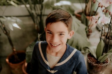 Niño sonriente con camisa de marinero, rodeado de plantas en macetas.