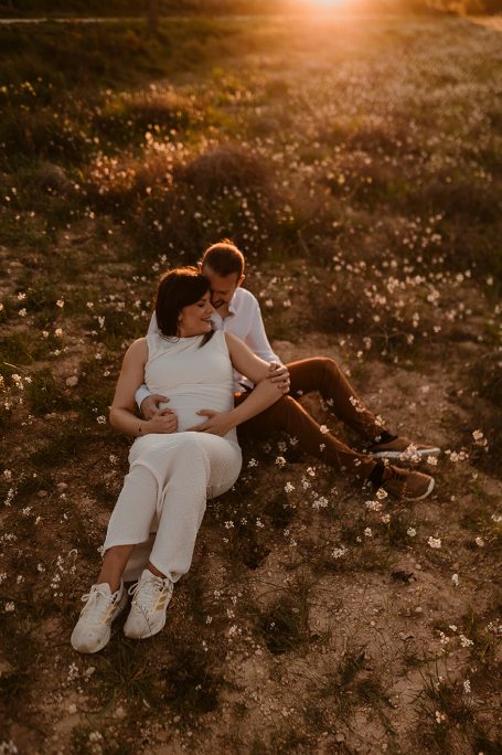 Pareja sentada en el suelo, rodeada de flores, con luz dorada del atardecer.