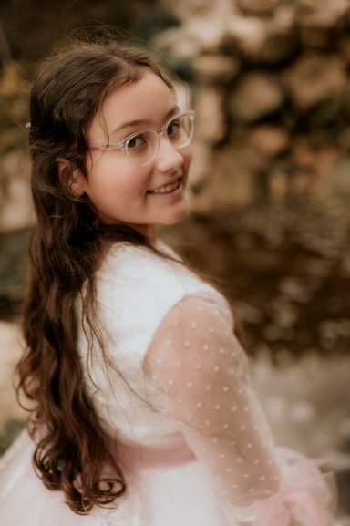 Niña con cabello largo y rizado, sonriendo, vestida con un vestido blanco y rosa.
