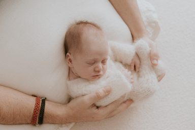 Un bebé dormido, envuelto en un suave tejido blanco, sostenido por manos adultas.