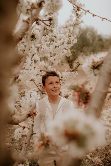 Niño sonriente rodeado de flores blancas en un campo.
