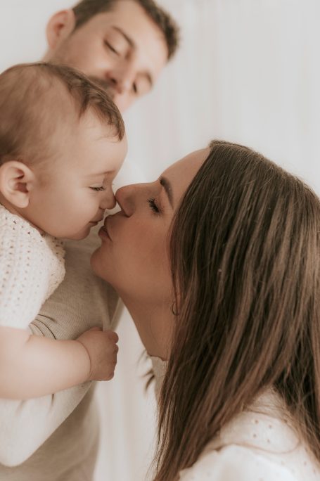 Mujer besando a un bebé mientras un niño observa sonriente.