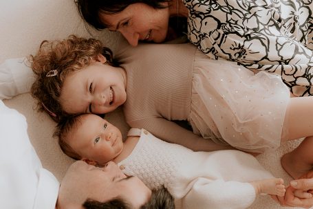 Familia acostada en una cama, riendo y disfrutando juntos.